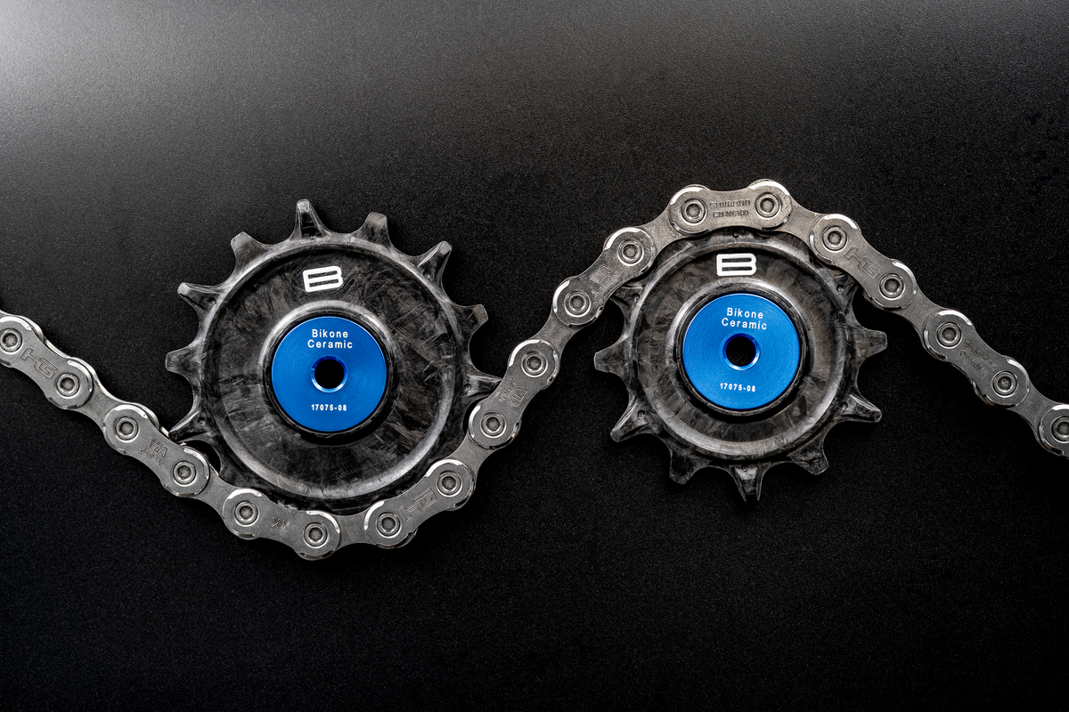 Bikone Forged Carbon Pulley Wheels, upper and lower pulleys threaded through a chain on a black background, road bike drivetrain components