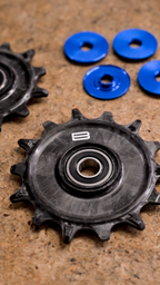 Bikone Forged Carbon Pulley Wheels, pulley on a workbench with its blue dust covers removed to show the bearing, road bike drivetrain components