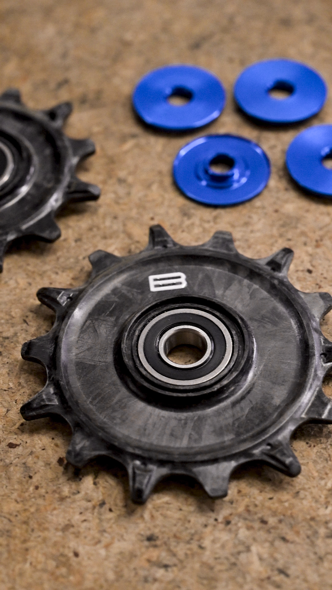 Bikone Forged Carbon Pulley Wheels, pulley on a workbench with its blue dust covers removed to show the bearing, road bike drivetrain components