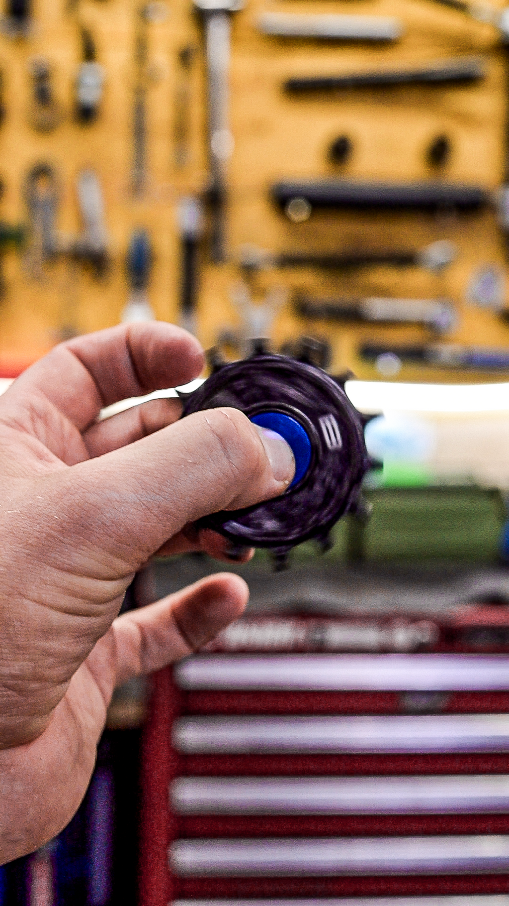 Bikone Forged Carbon Pulley Wheels, pulley spinning in a mechanic's hand in front of a workshop tool wall, road bike drivetrain components